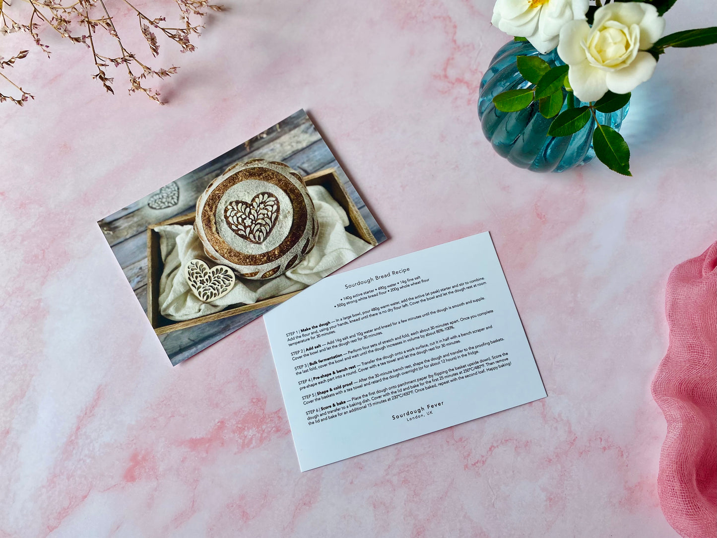 Card with heart designs on a pink surface next to flowers